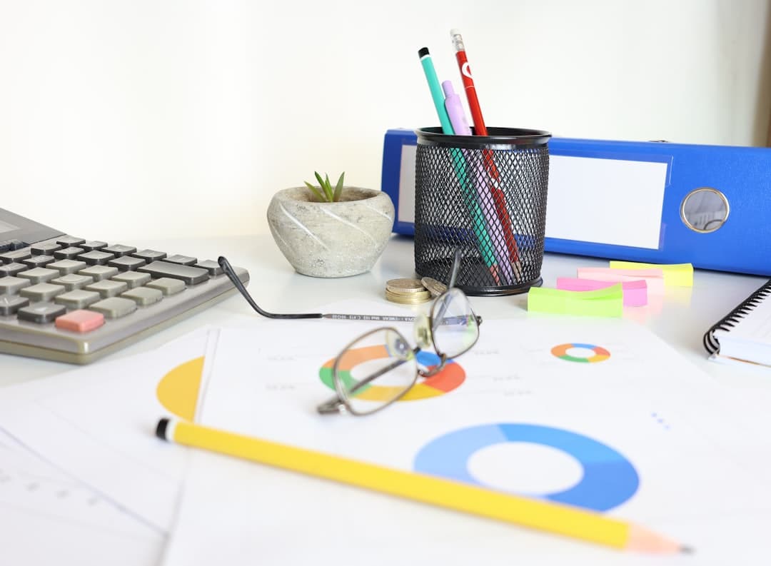 A desk with a calculator, glasses, charts, and office supplies
