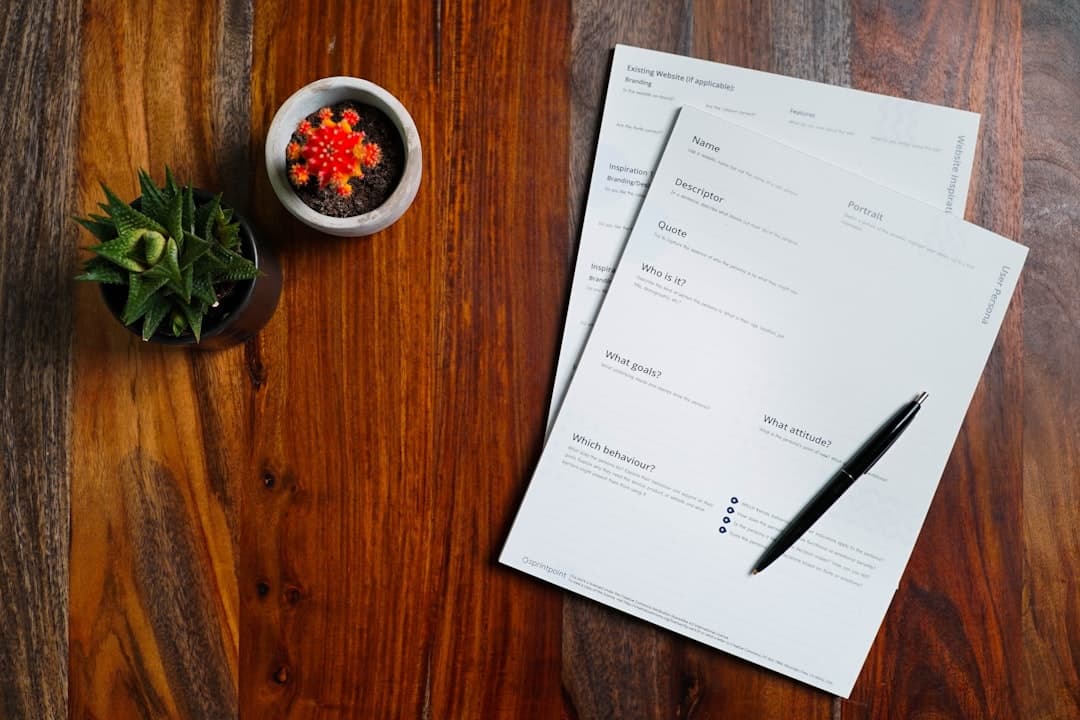 A wooden desk with papers and a pen